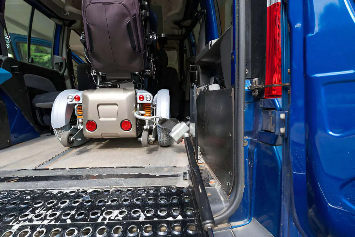 Blue NYC Wheelchair van with deployed ramp at JFK Terminal, assisting a passenger in a power wheelchair